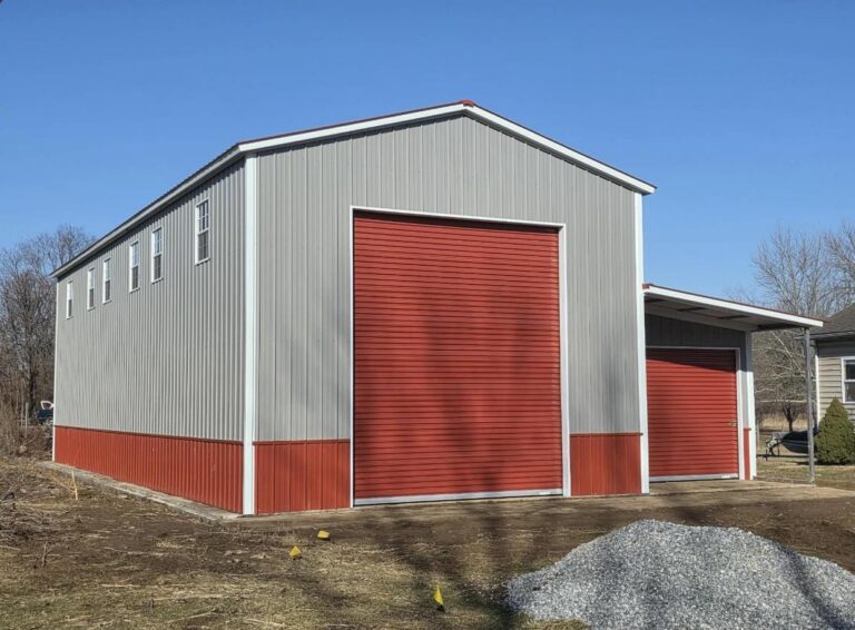 Gray steel barn with red wainscot and a tall red roll-up door