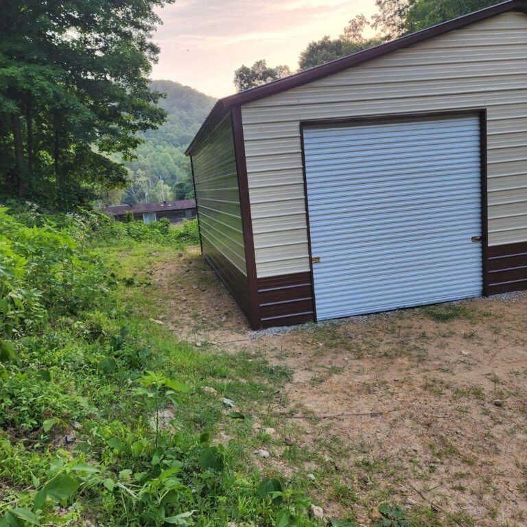 Gray metal garage with blue roll-up door beside mature trees
